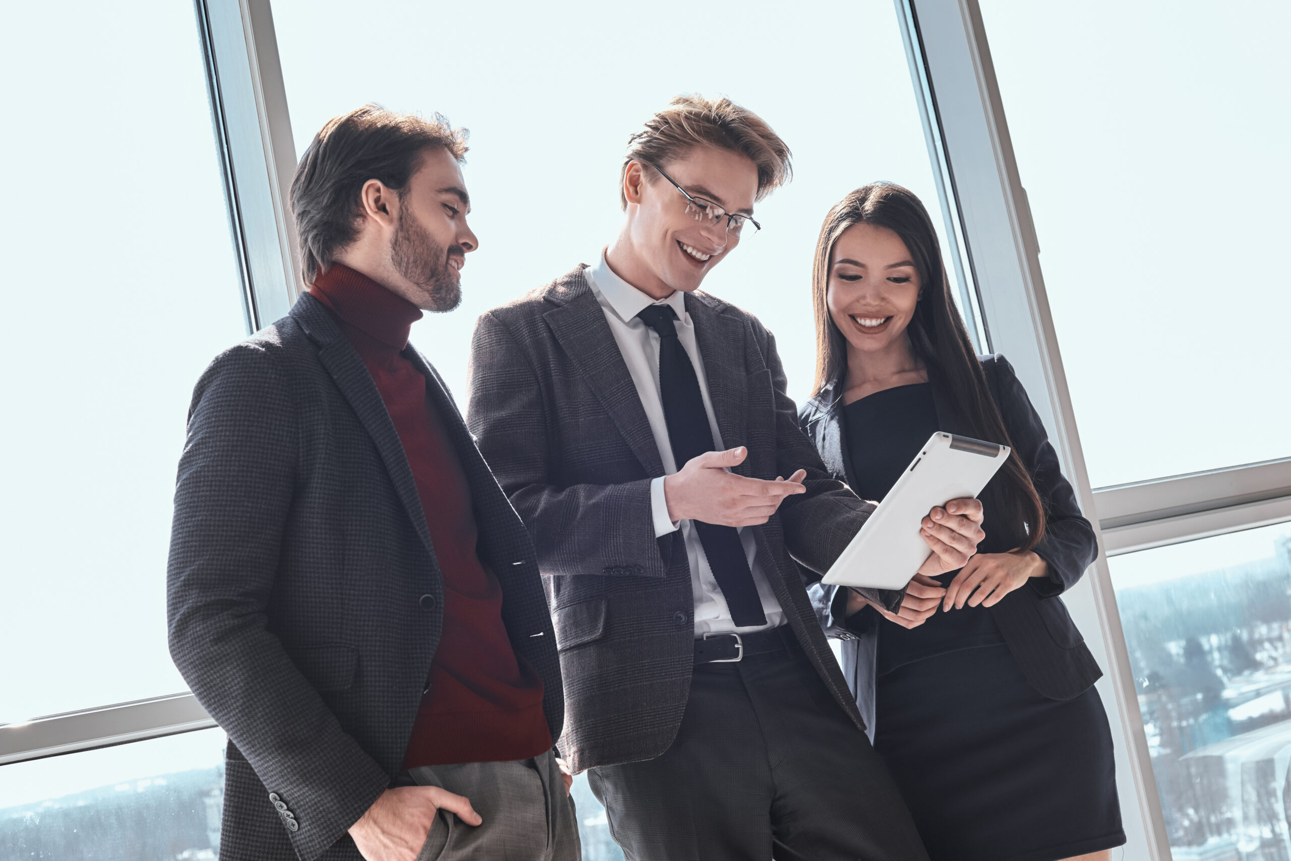 Businesspeople at office working together standing man showing p Businessmen and businesswoman at office working together standing man showing project plan on digital tablet to collegues smiling joyful discussing