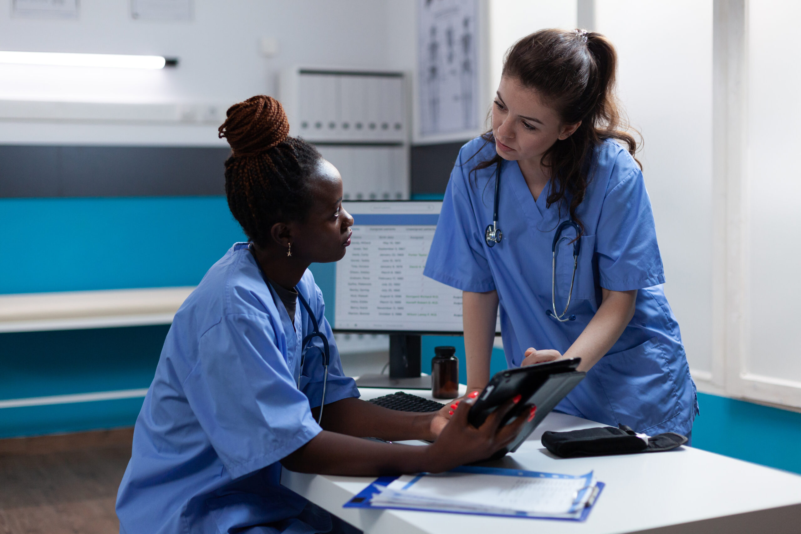 Multi-ethnic medical nurses analyzing sickness symptoms Multi-ethnic medical nurses analyzing sickness symptoms discussing healthcare treatment working in hospital office. Teamworks checking pharmaceutical medication on tablet computer sitting at desk